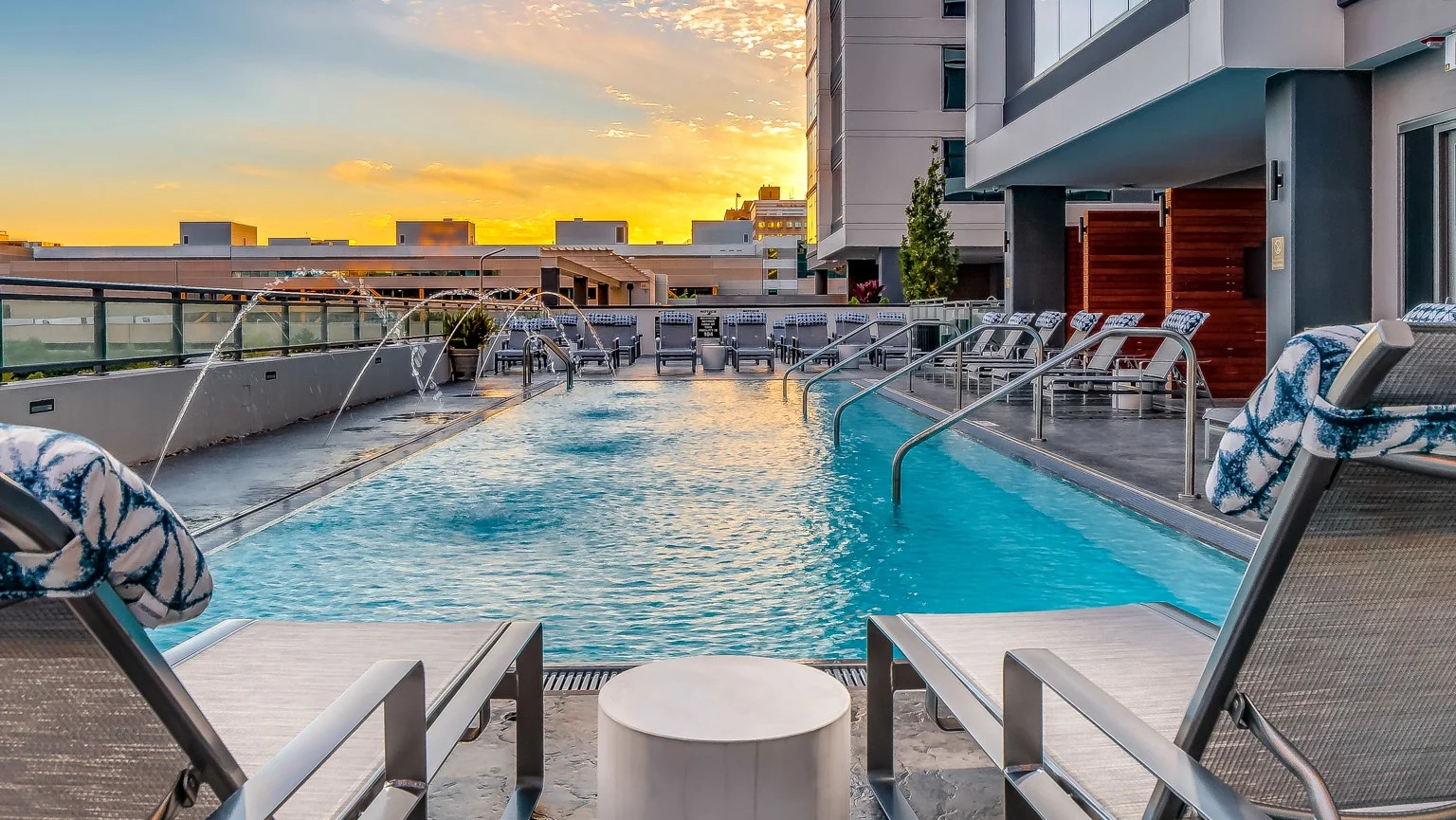 Stunning sunset view from the rooftop pool lounge at The Grand Central Apartments in Chicago, featuring lounge chairs and illuminated water