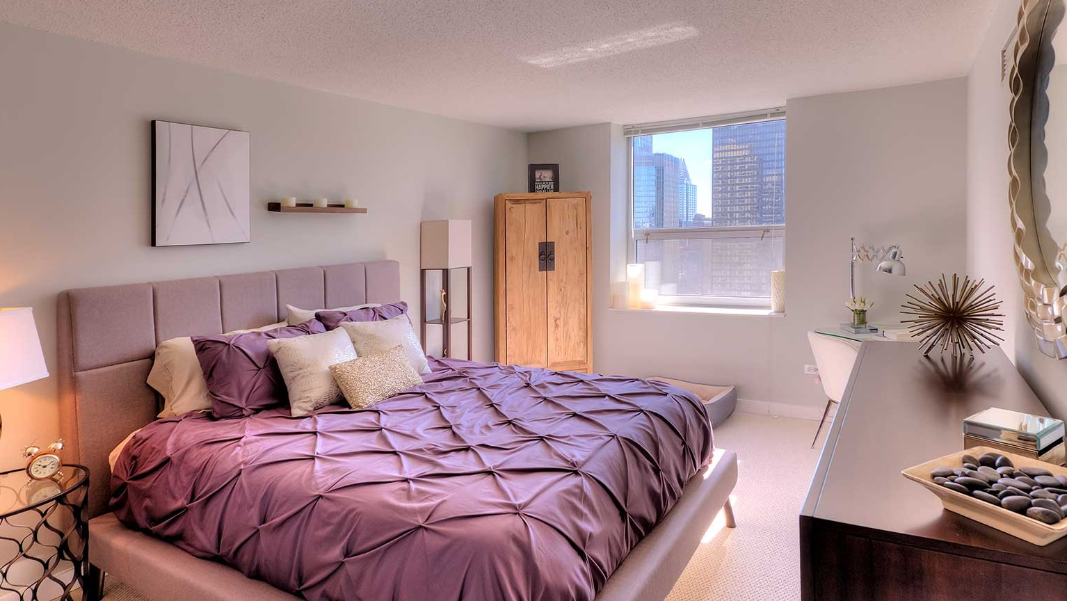 Spacious bedroom with a comfortable bed, stylish decor, and city views from the window at Grand Plaza apartments in Chicago