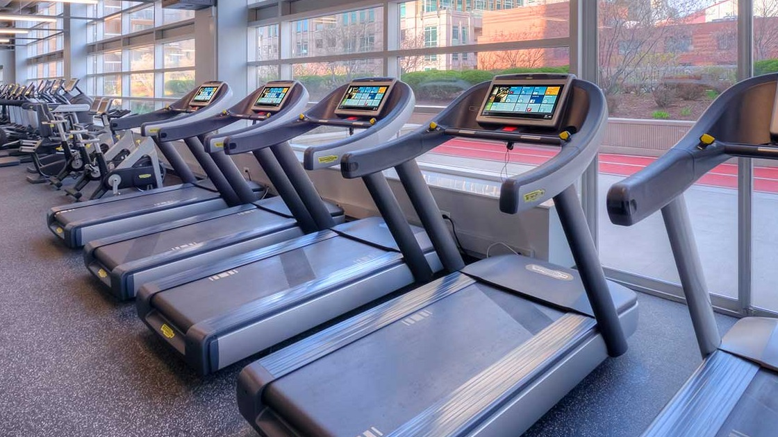 Modern fitness center with a row of treadmills and large windows offering city views at Grand Plaza apartments in Chicago
