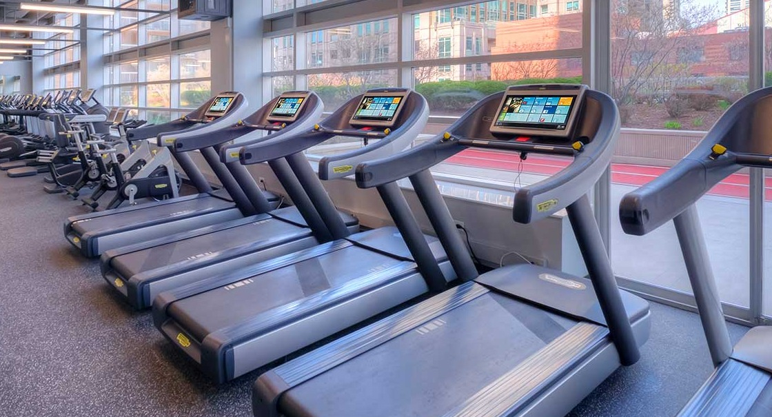 Modern fitness center with a row of treadmills and large windows offering city views at Grand Plaza apartments in Chicago
