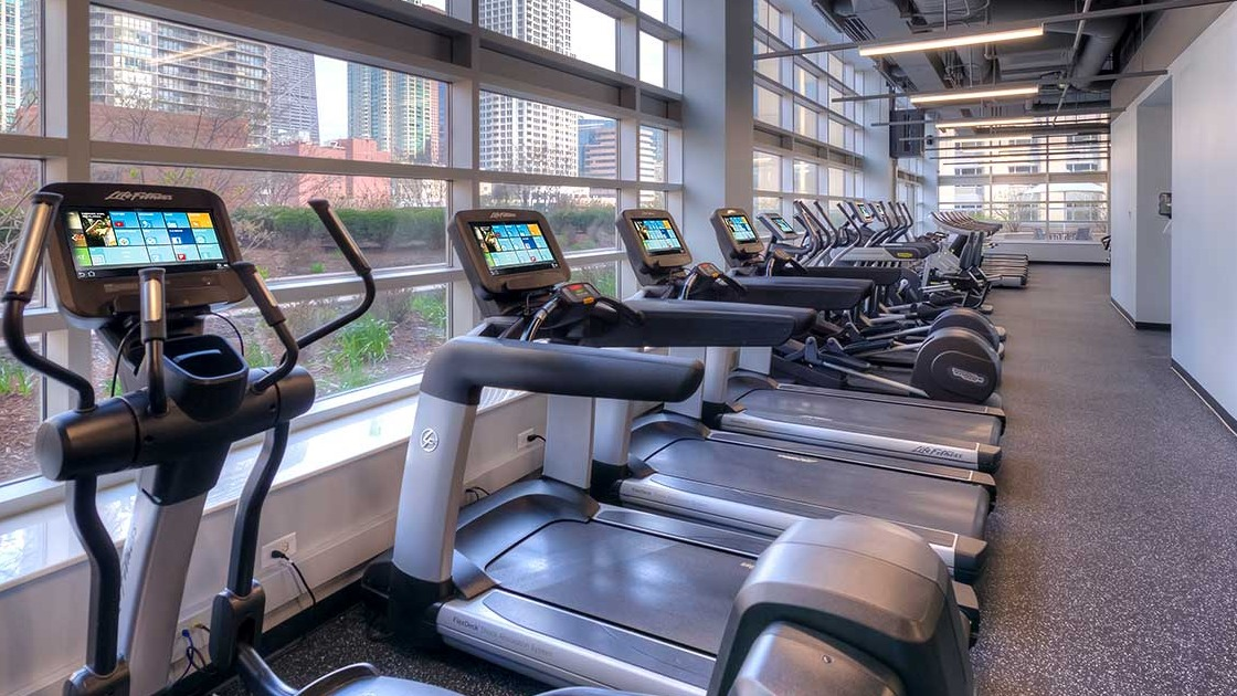 Spacious gym with various exercise equipment and abundant natural light from large windows at Grand Plaza apartments in Chicago
