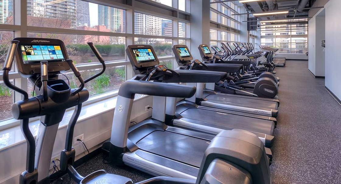 Spacious gym with various exercise equipment and abundant natural light from large windows at Grand Plaza apartments in Chicago