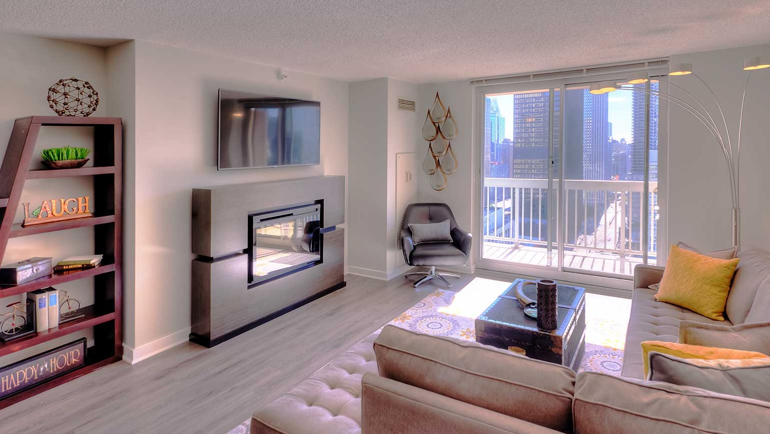 Stylish living room with a cozy fireplace, TV, and large windows offering city views at Grand Plaza apartments in Chicago