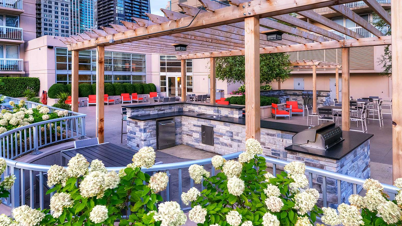 Outdoor grilling area with modern grills, a shaded pergola, and elegant landscaping at Grand Plaza apartments in Chicago