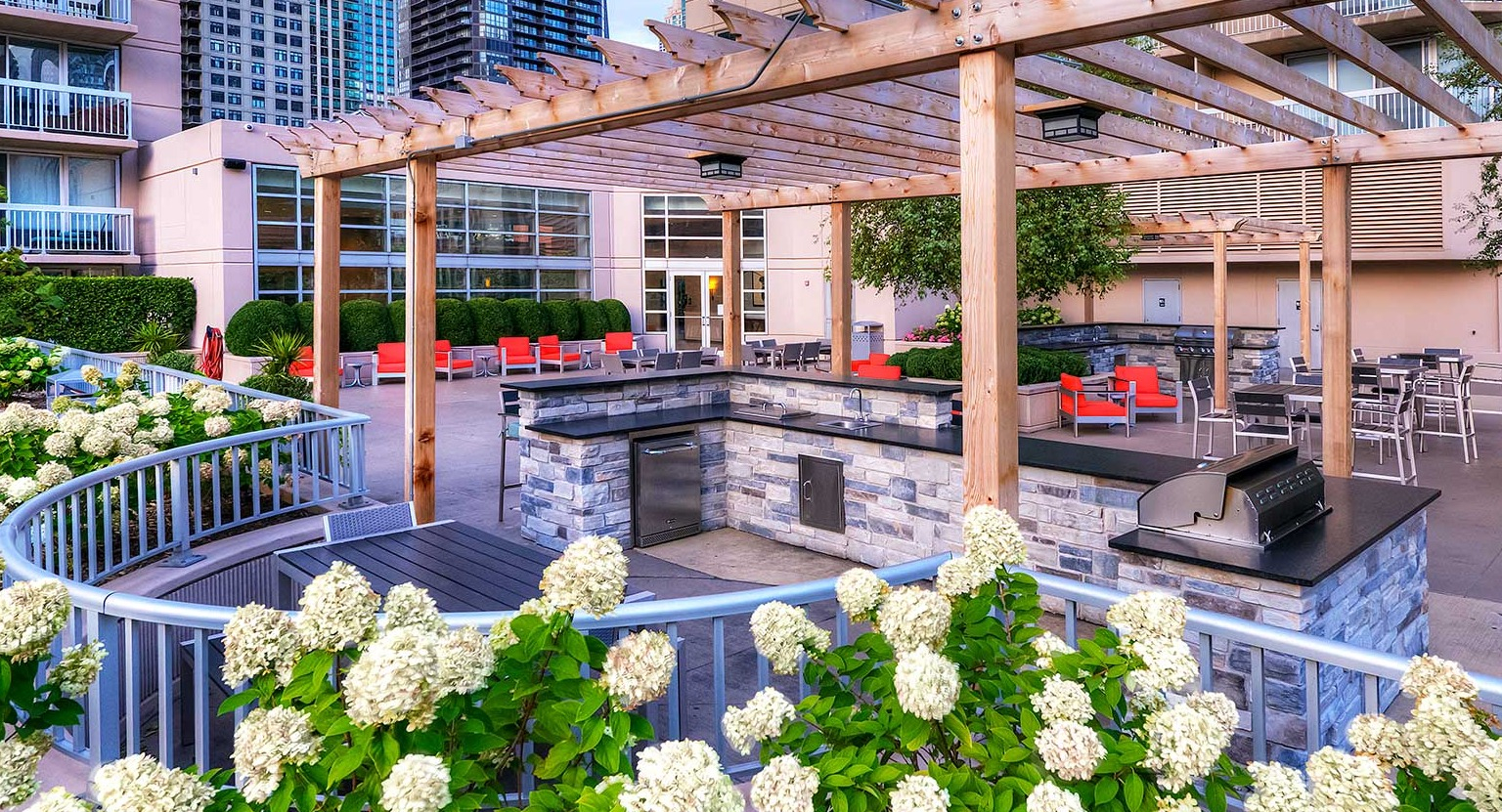 Outdoor grilling area with modern grills, a shaded pergola, and elegant landscaping at Grand Plaza apartments in Chicago