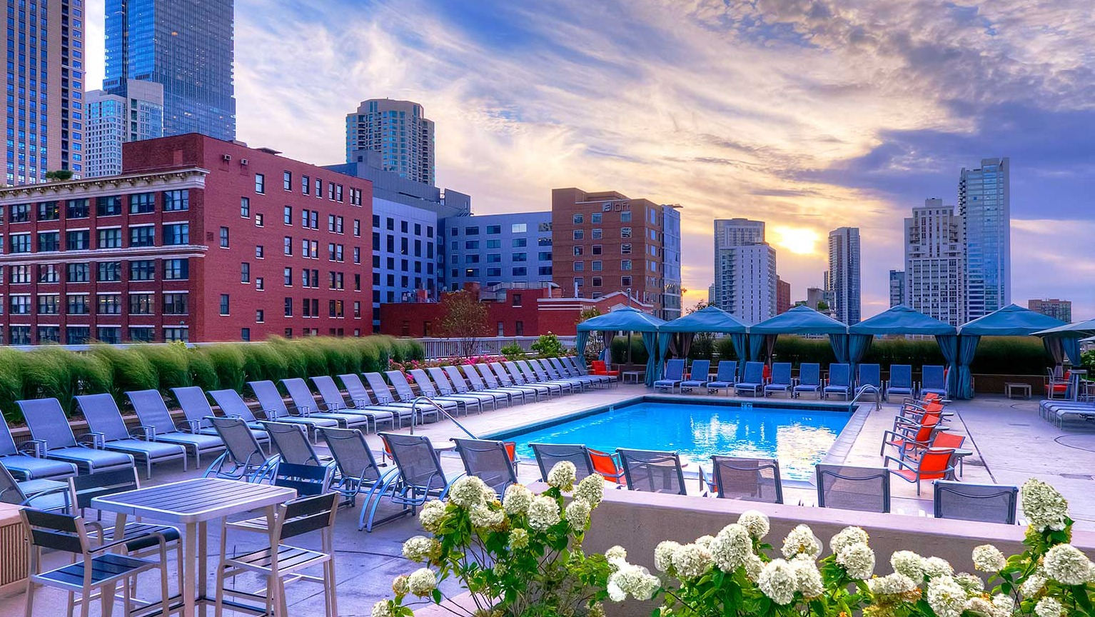 Stunning outdoor swimming pool with lounge chairs, cabanas, and a beautiful sunset city skyline at Grand Plaza in Chicago
