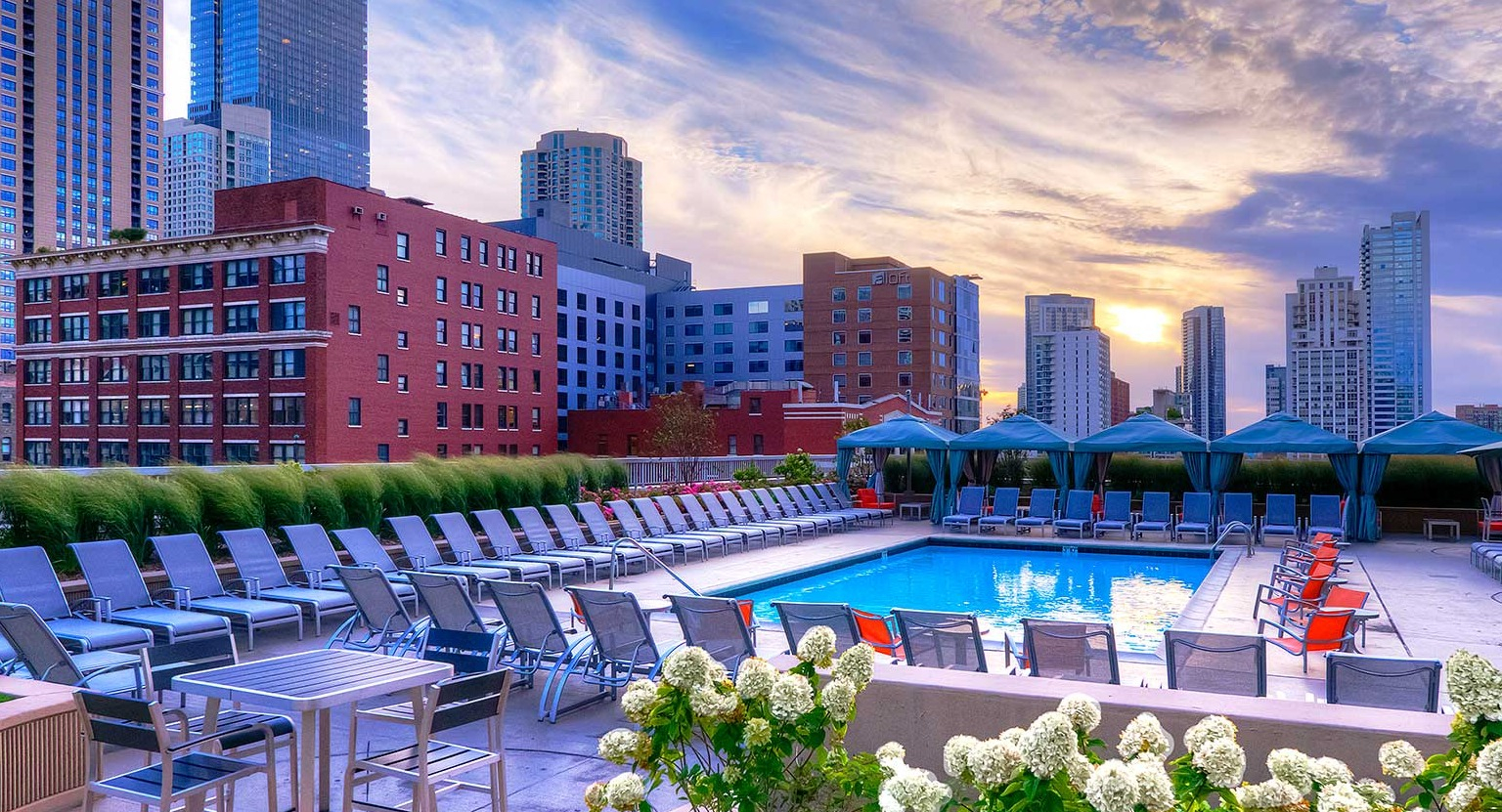 Stunning outdoor swimming pool with lounge chairs, cabanas, and a beautiful sunset city skyline at Grand Plaza in Chicago
