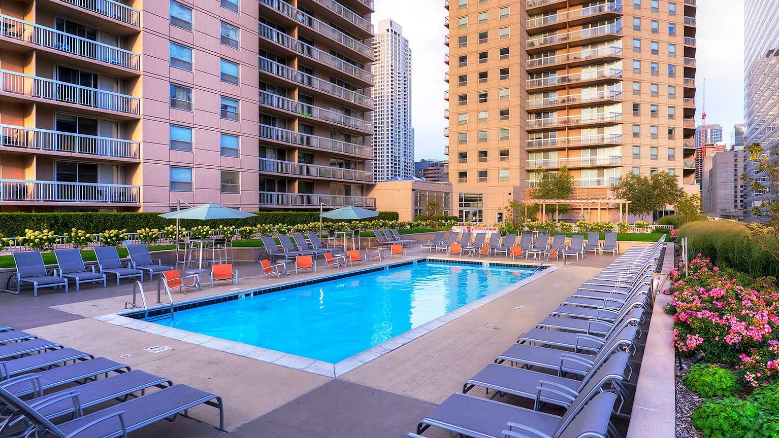 Serene pool deck surrounded by lush landscaping, lounge chairs, and city views at Grand Plaza apartments in Chicago