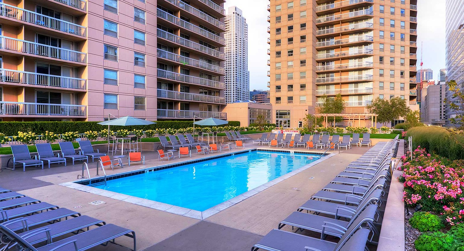 Serene pool deck surrounded by lush landscaping, lounge chairs, and city views at Grand Plaza apartments in Chicago