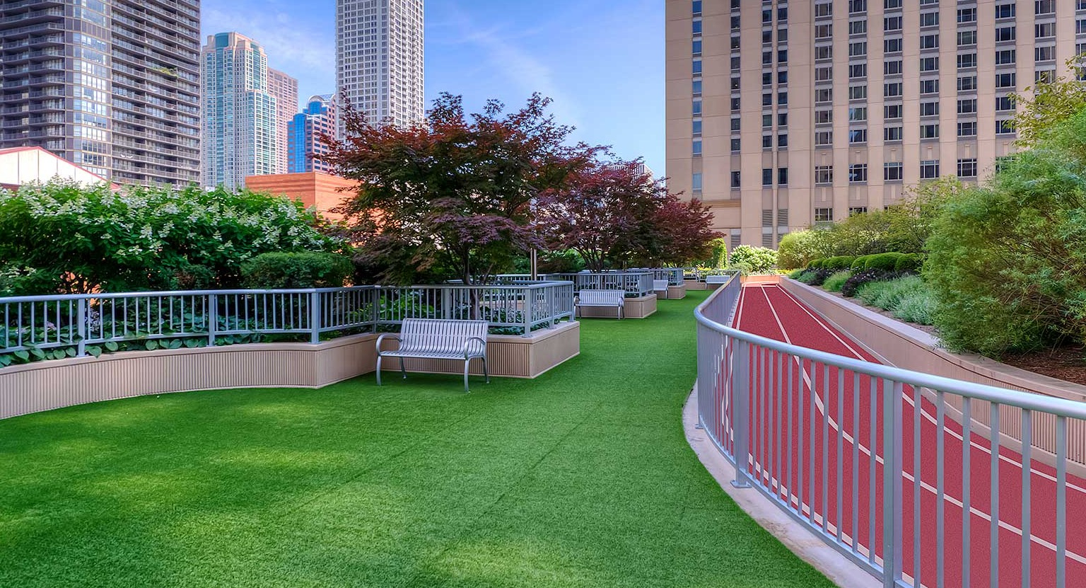Outdoor running track alongside a green turf area, surrounded by lush landscaping and city views at Grand Plaza in Chicago