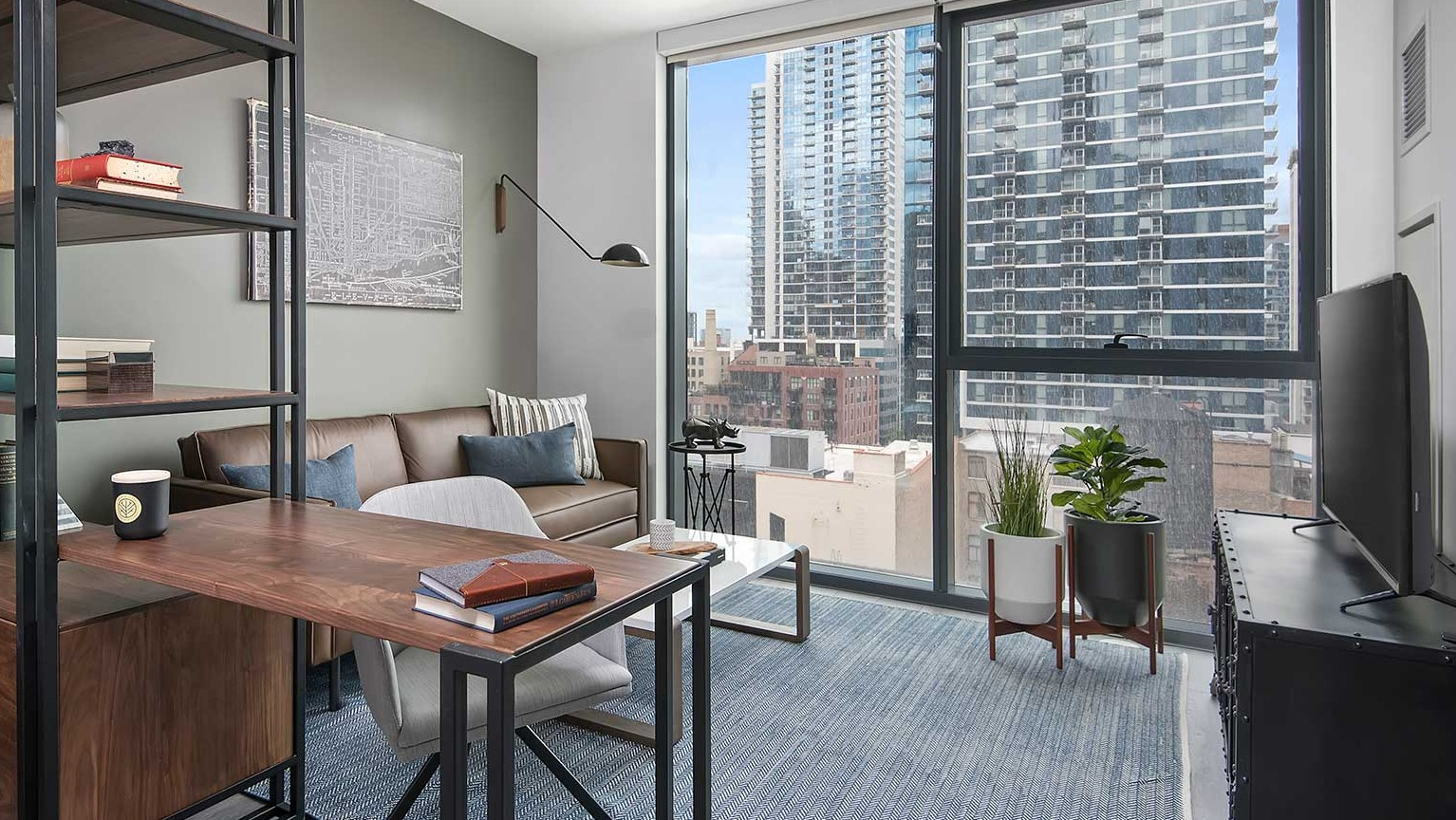 A stylish apartment den at Hubbard 221, perfect for a home office, with a desk, shelving, and city views