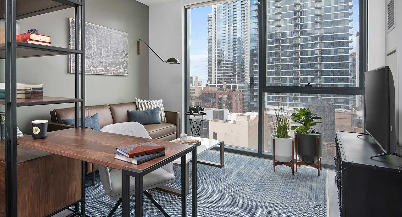 A stylish apartment den at Hubbard 221, perfect for a home office, with a desk, shelving, and city views