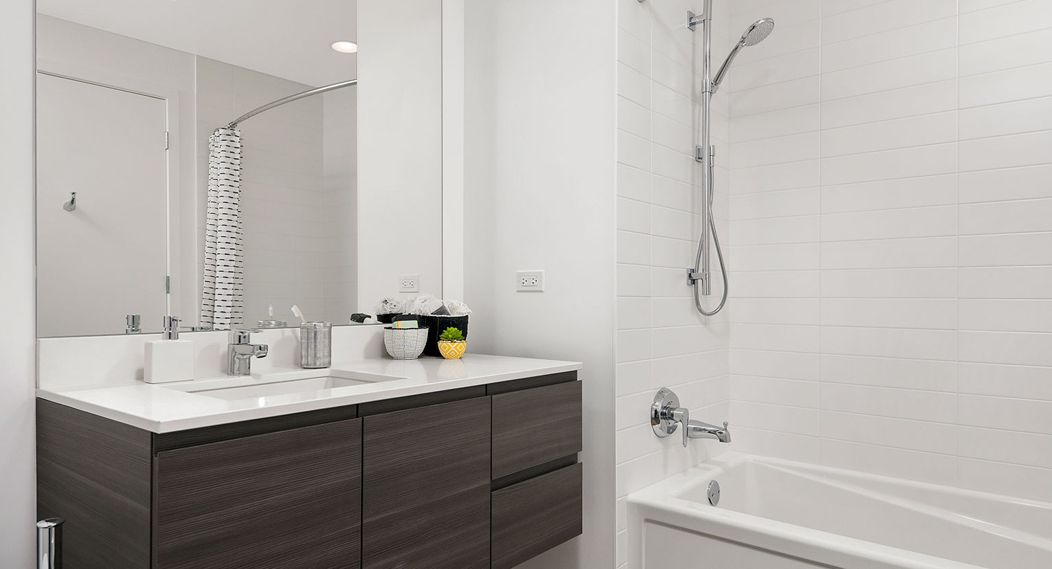 A clean and modern bathroom at Hubbard 221 featuring a dark wood vanity, white subway tile, and a spacious bathtub