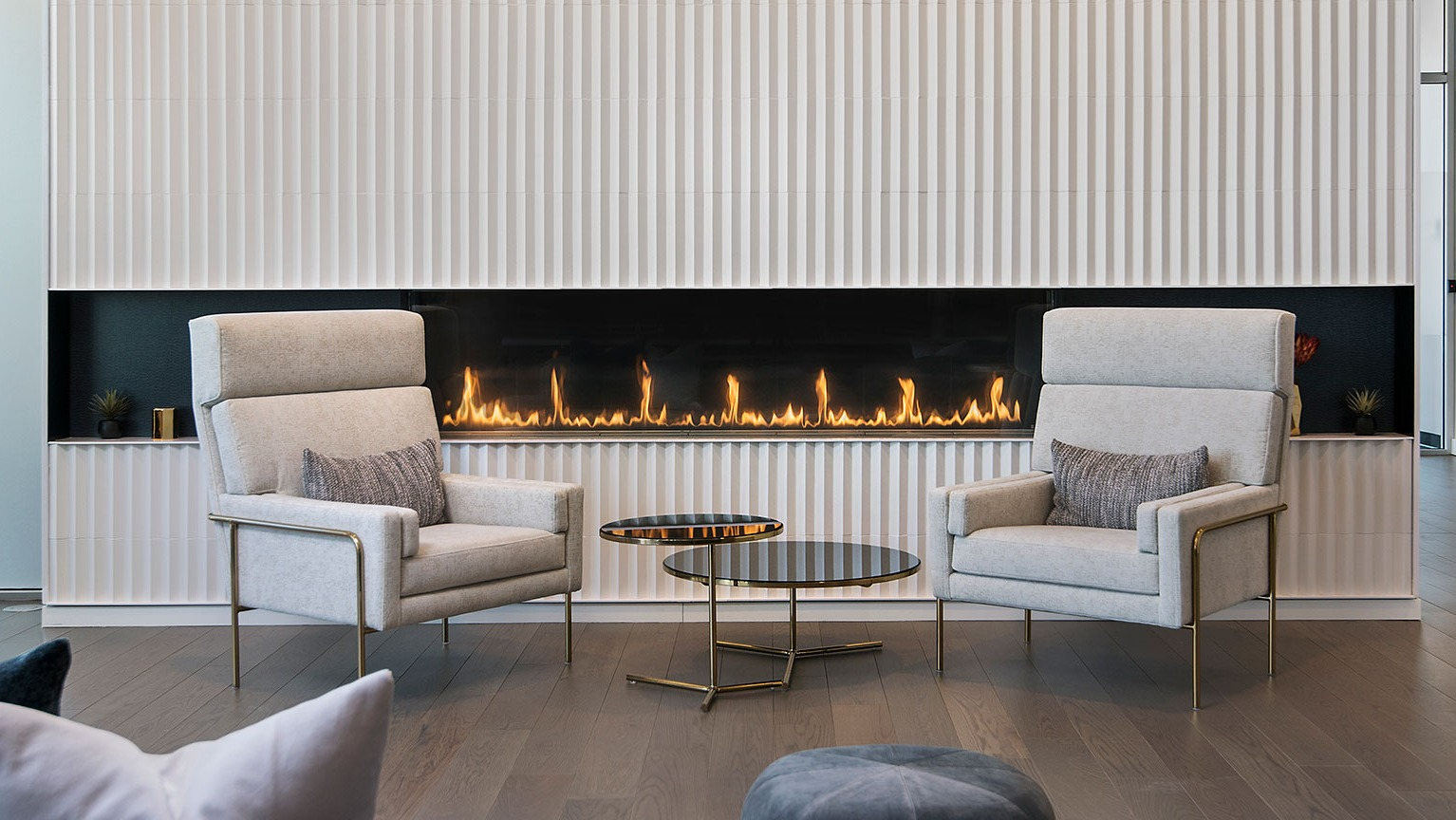 A cozy lounge area at Hubbard 221 featuring a modern linear fireplace, elegant armchairs, and warm lighting