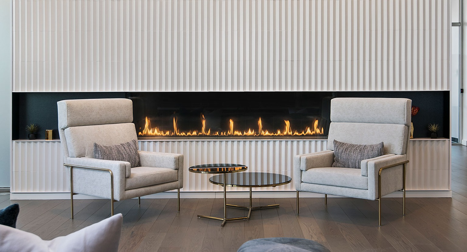 A cozy lounge area at Hubbard 221 featuring a modern linear fireplace, elegant armchairs, and warm lighting