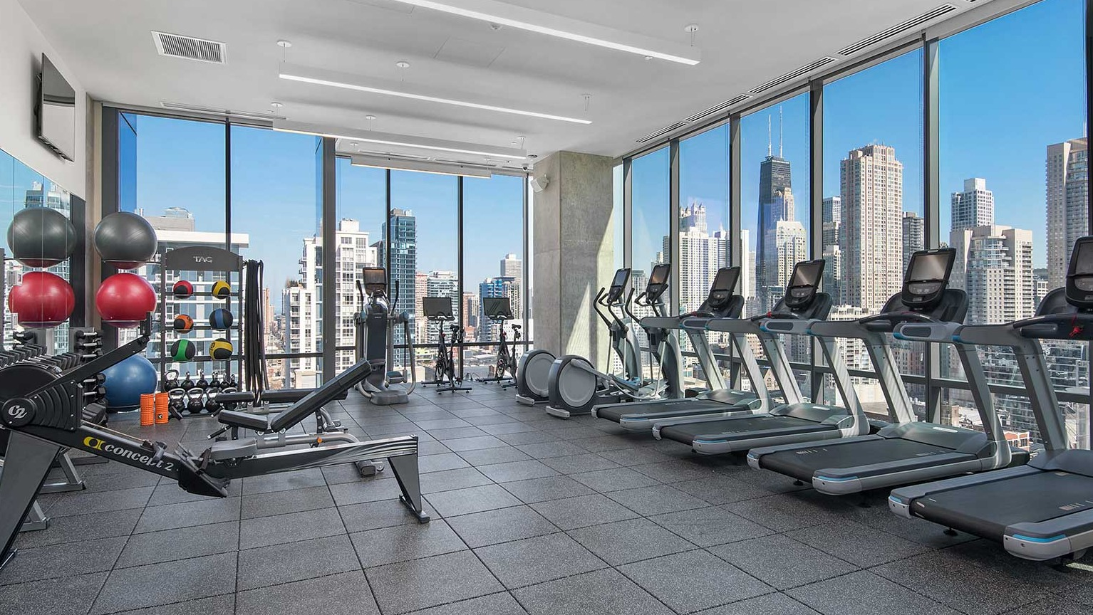 A modern fitness center at Hubbard 221 offering diverse exercise equipment and stunning city views from large windows