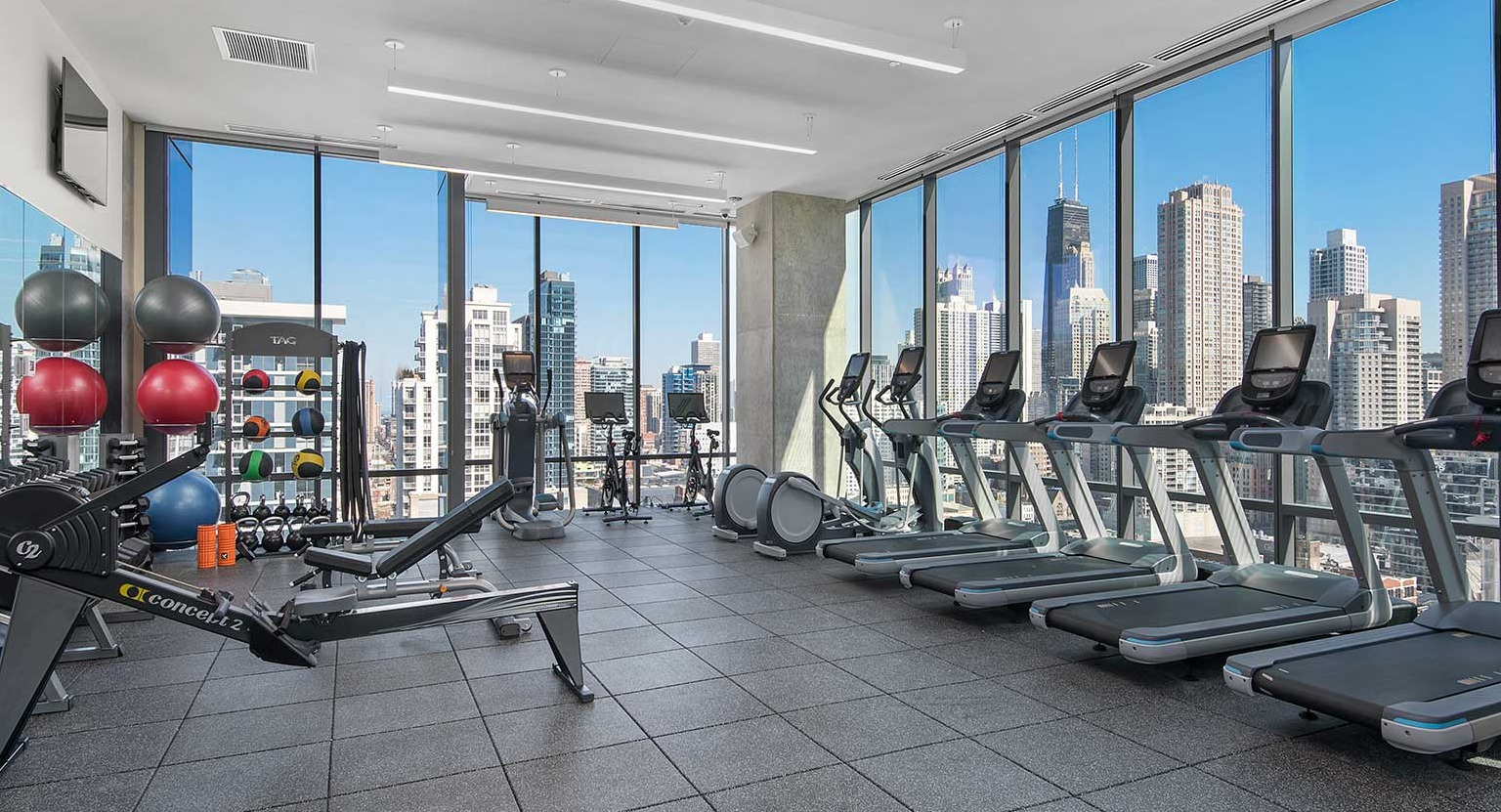 A modern fitness center at Hubbard 221 offering diverse exercise equipment and stunning city views from large windows