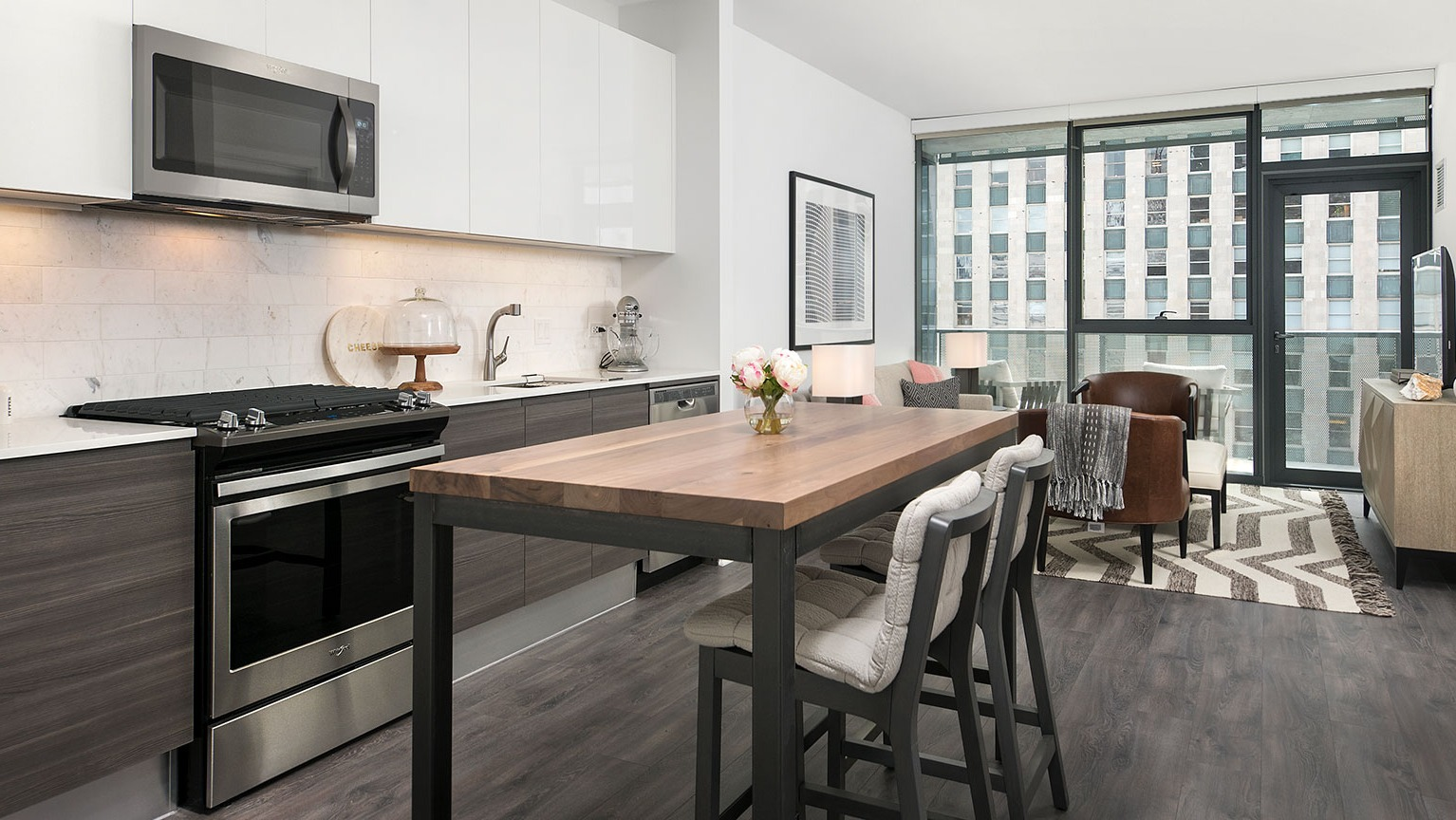 A contemporary kitchen at Hubbard 221 with white cabinets, dark wood accents, and a casual dining table with stools