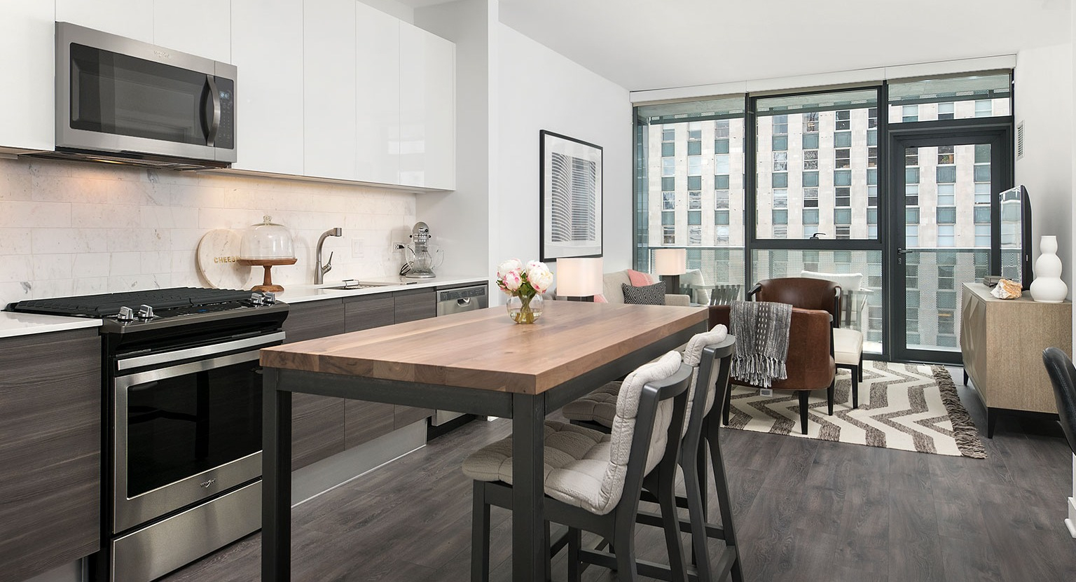 A contemporary kitchen at Hubbard 221 with white cabinets, dark wood accents, and a casual dining table with stools