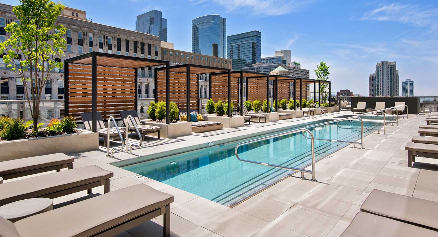 A serene outdoor pool area at Hubbard 221 with numerous lounge chairs, pergolas, and city buildings in the background