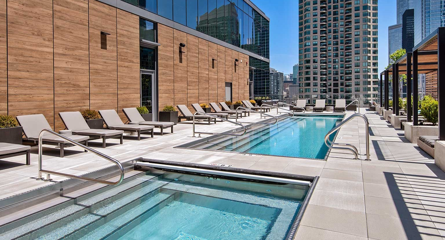 A luxurious rooftop pool and spa area at Hubbard 221 with lounge chairs and stunning city architecture in Chicago