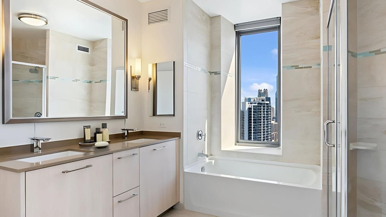 Elegant bathroom featuring a double vanity, a deep soaking tub, and a separate shower with a city view at Hubbard Place in Chicago