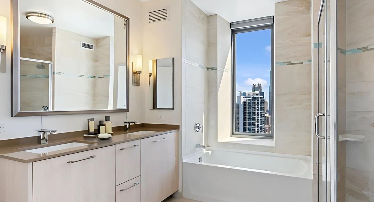 Elegant bathroom featuring a double vanity, a deep soaking tub, and a separate shower with a city view at Hubbard Place in Chicago