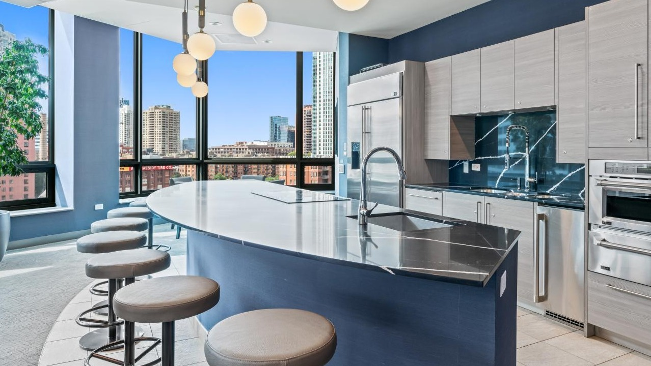 Luxurious community kitchen with a large curved island, bar seating, and stunning city views at Hubbard Place in Chicago