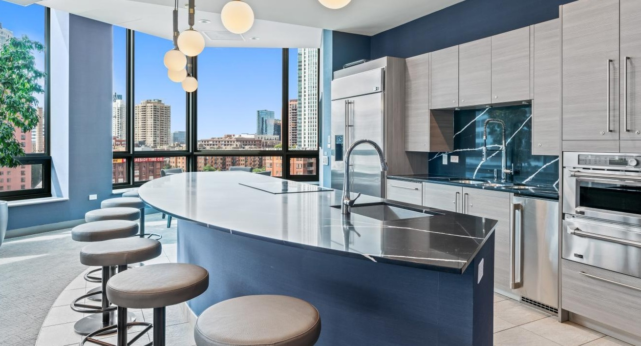 Luxurious community kitchen with a large curved island, bar seating, and stunning city views at Hubbard Place in Chicago