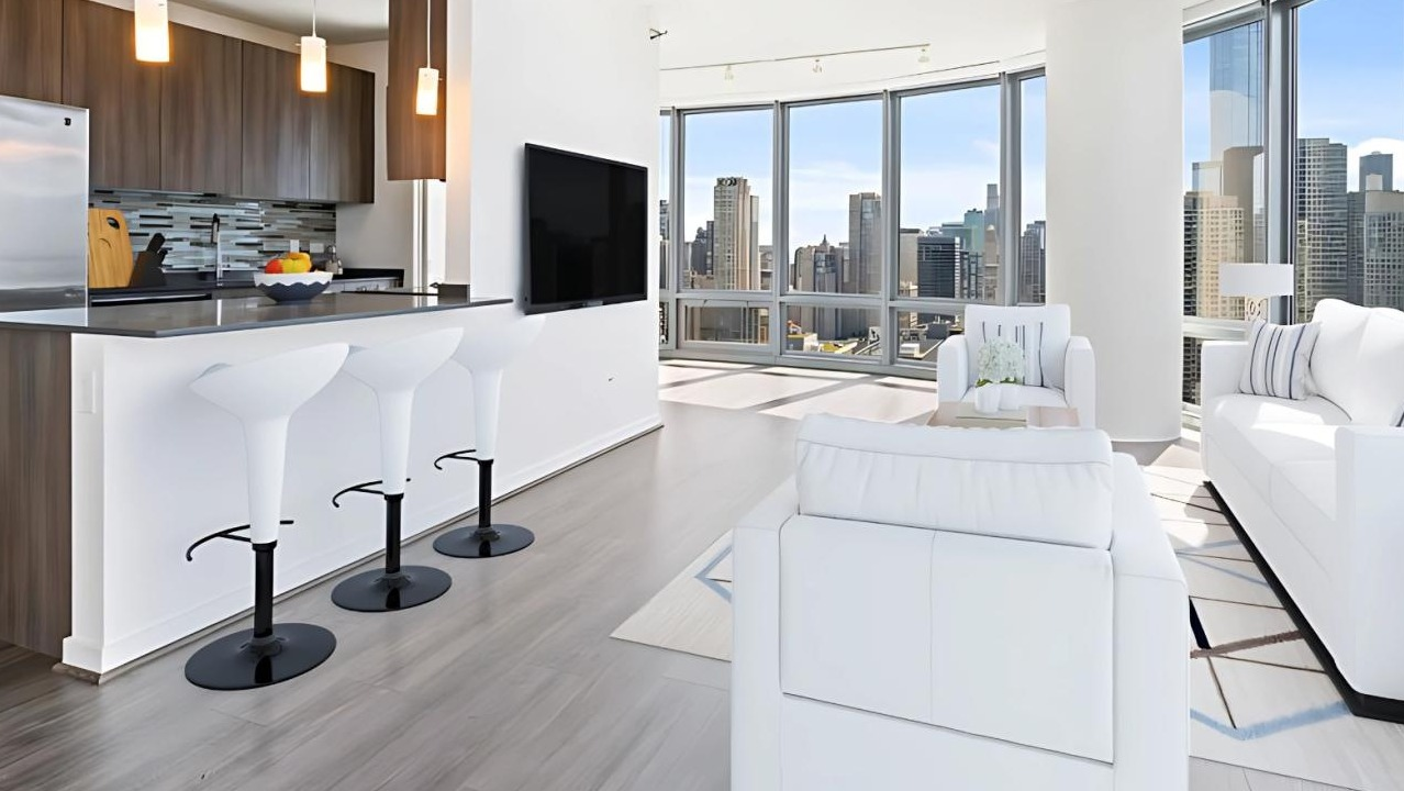 Bright open-concept kitchen and living room with white furniture, a breakfast bar, and large windows offering city views at Hubbard Place in Chicago