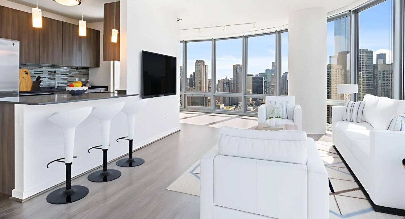 Bright open-concept kitchen and living room with white furniture, a breakfast bar, and large windows offering city views at Hubbard Place in Chicago
