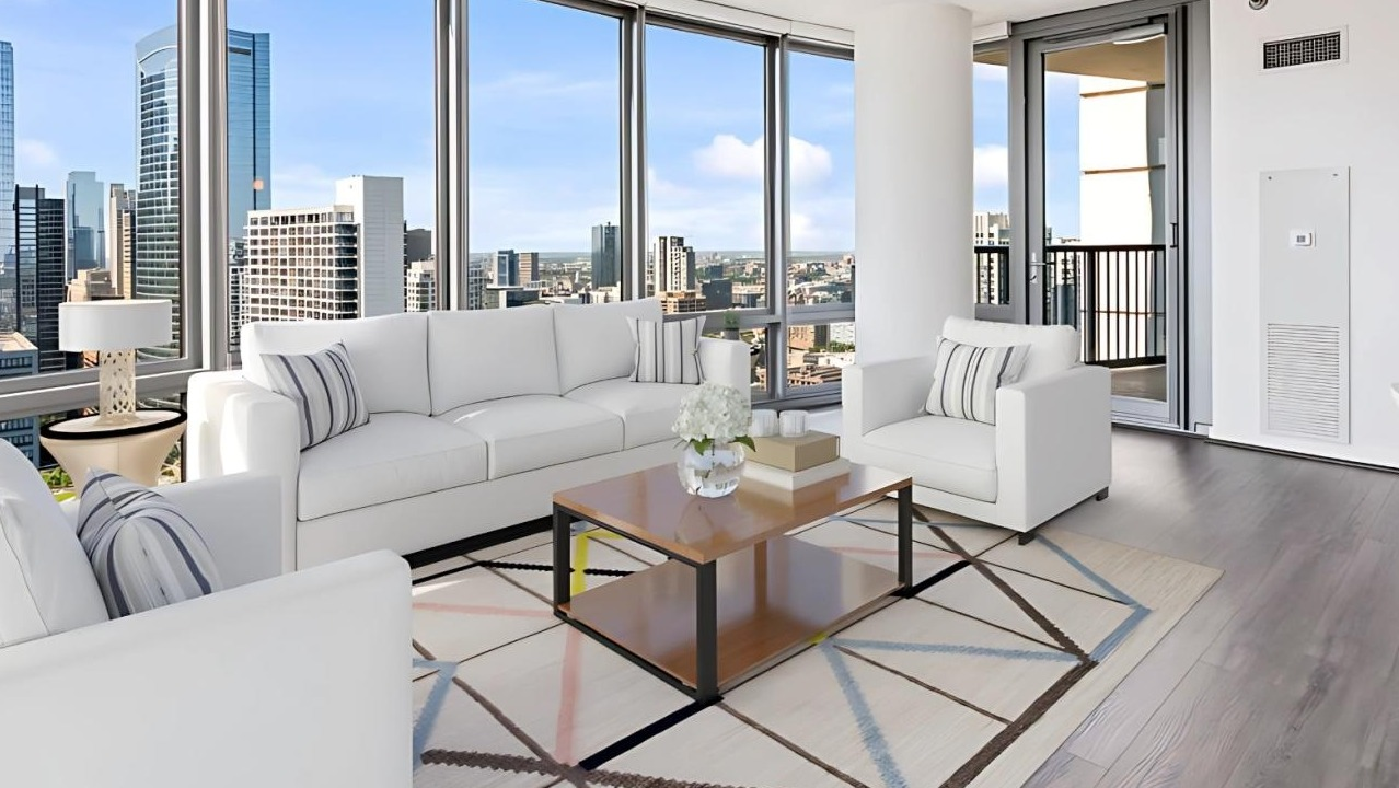 Spacious living room with white sofas, a stylish rug, and a balcony offering expansive city views at Hubbard Place in Chicago