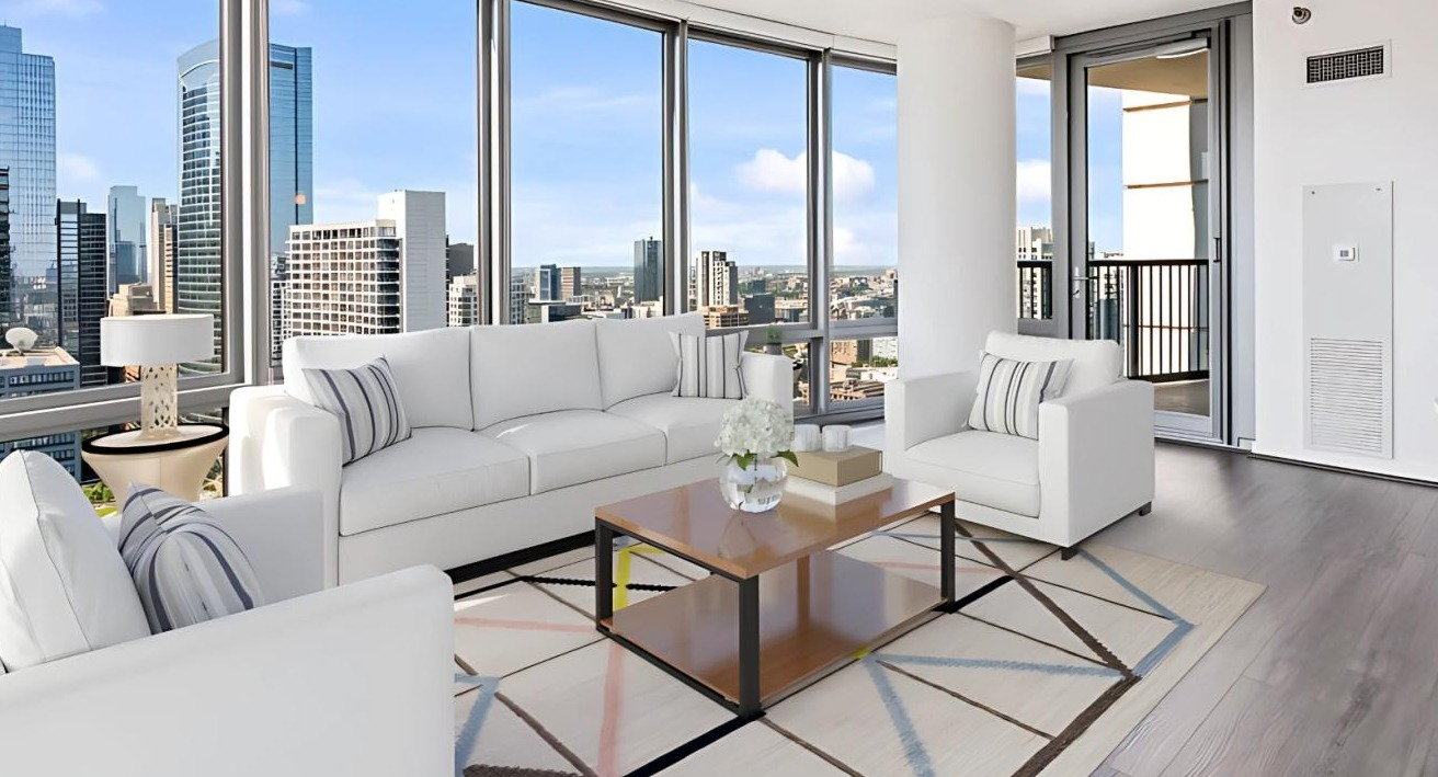 Spacious living room with white sofas, a stylish rug, and a balcony offering expansive city views at Hubbard Place in Chicago