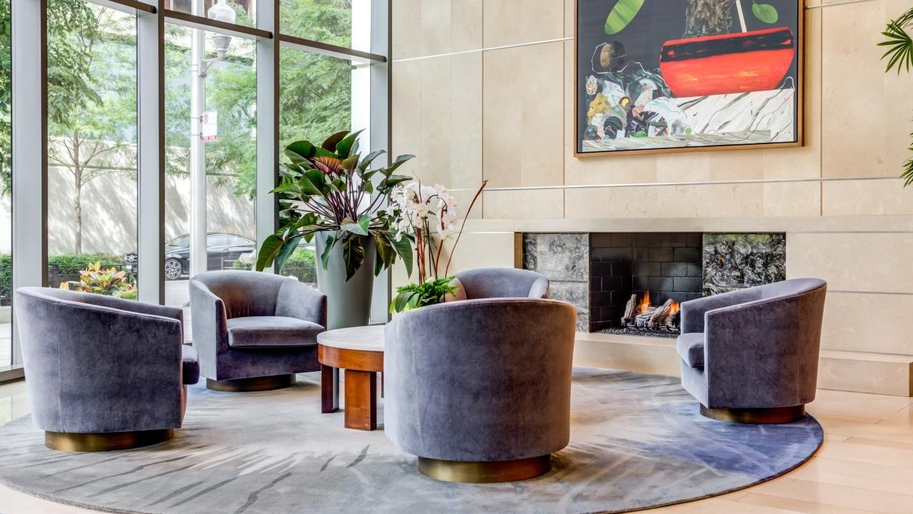 Elegant lobby seating area with comfortable chairs arranged around a fireplace and a captivating art piece at Hubbard Place in Chicago