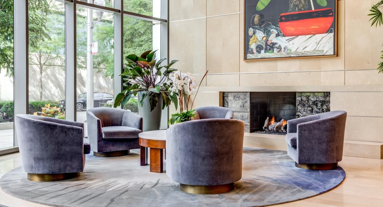 Elegant lobby seating area with comfortable chairs arranged around a fireplace and a captivating art piece at Hubbard Place in Chicago