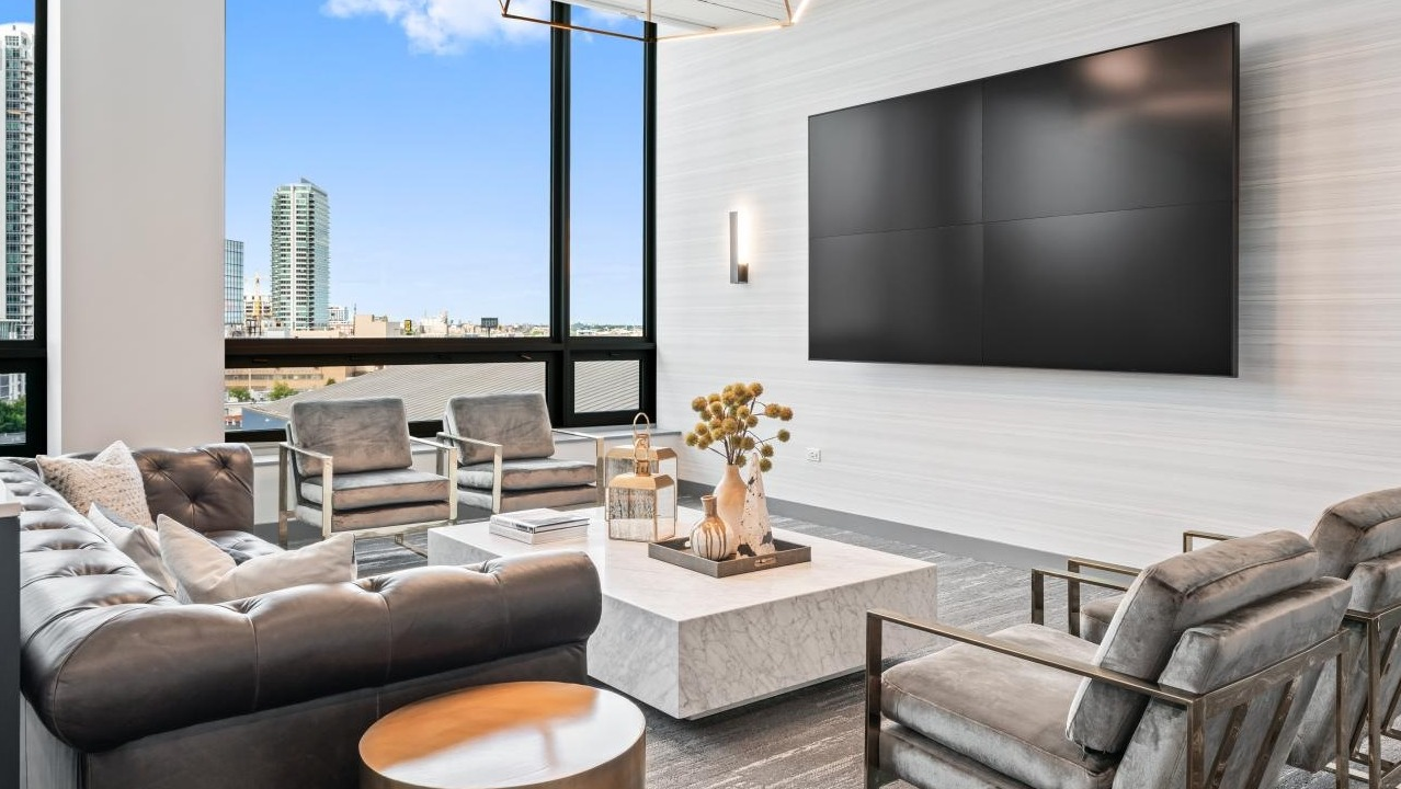 Modern resident lounge with comfortable seating, a large media screen, and expansive city views at Hubbard Place in Chicago