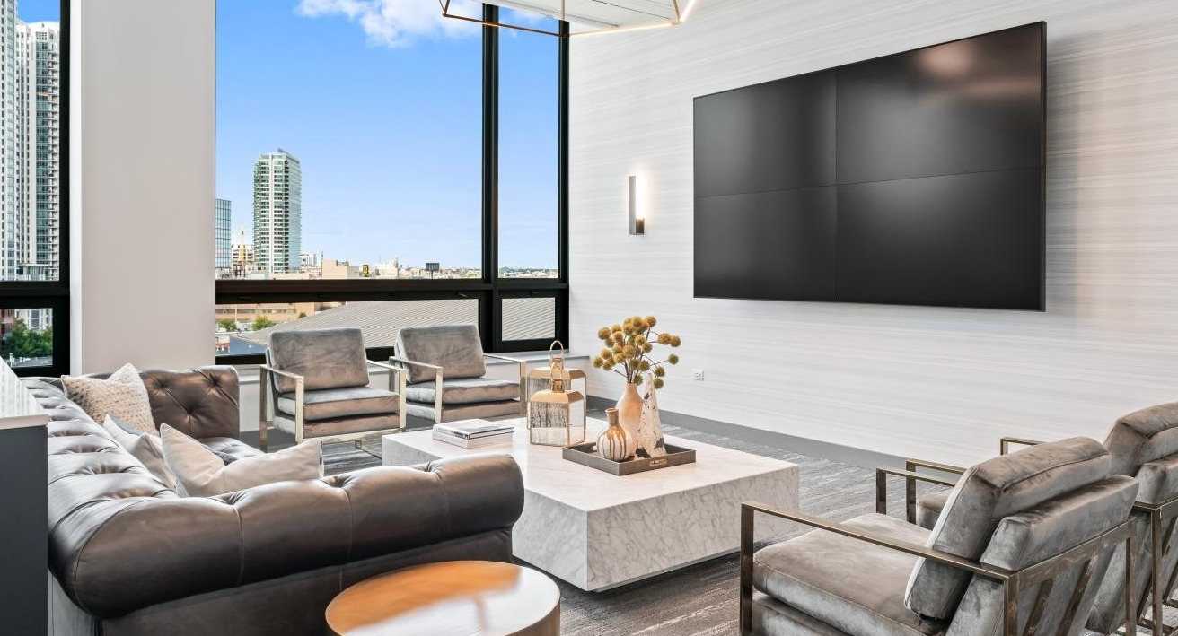 Modern resident lounge with comfortable seating, a large media screen, and expansive city views at Hubbard Place in Chicago