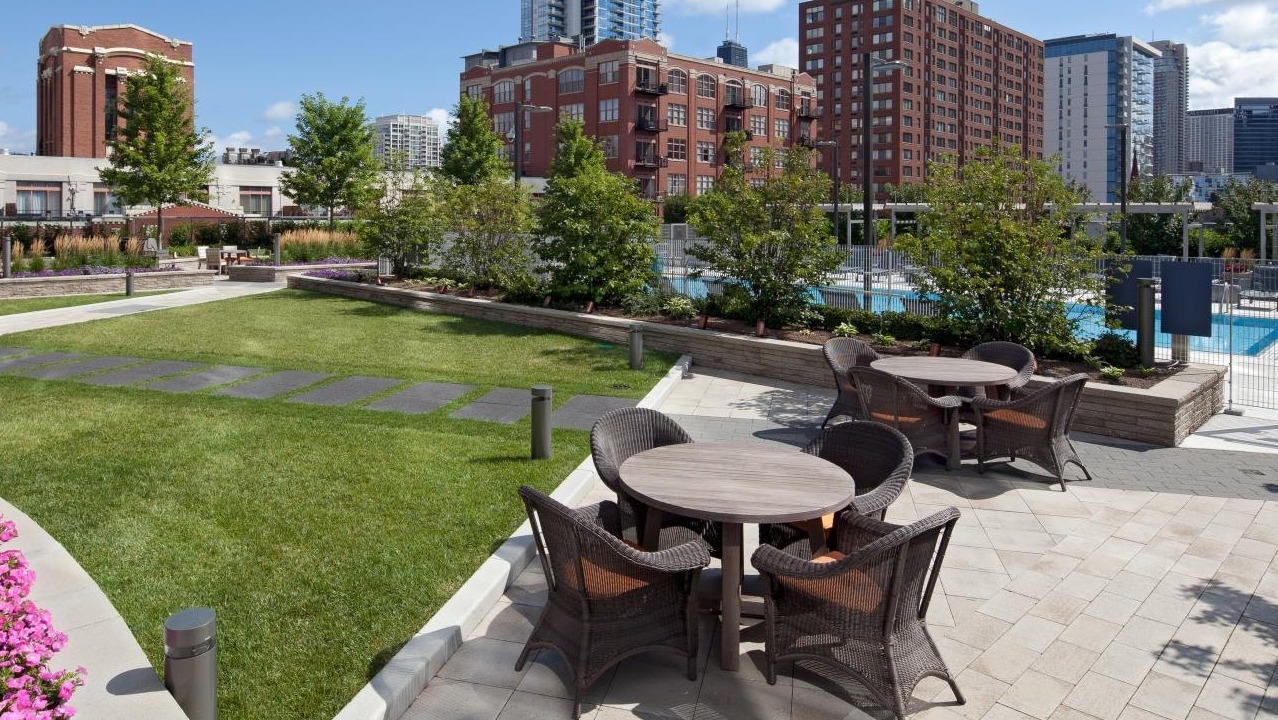 Landscaped outdoor courtyard with dining tables, seating areas, and a glimpse of the pool at Hubbard Place in Chicago