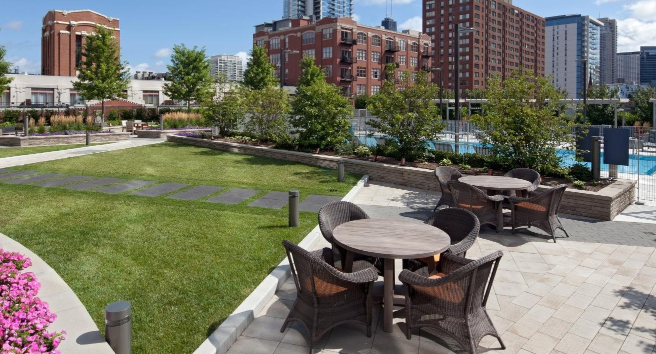 Landscaped outdoor courtyard with dining tables, seating areas, and a glimpse of the pool at Hubbard Place in Chicago