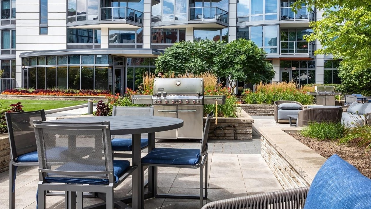 Outdoor courtyard with barbecue grills, dining tables, and comfortable seating, surrounded by lush landscaping at Hubbard Place in Chicago