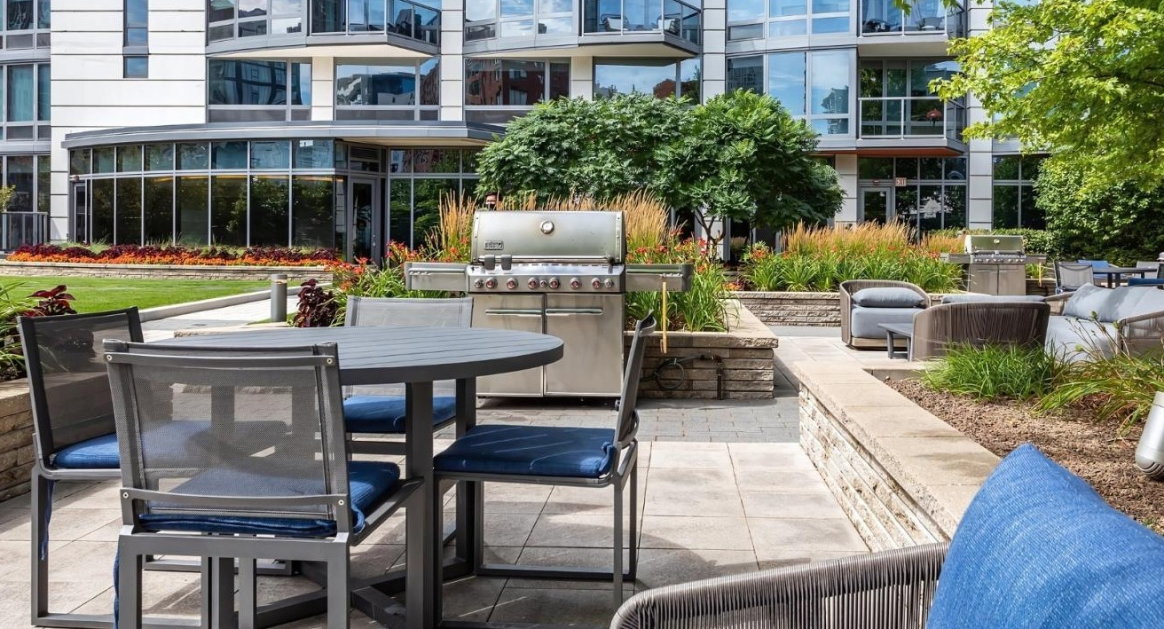 Outdoor courtyard with barbecue grills, dining tables, and comfortable seating, surrounded by lush landscaping at Hubbard Place in Chicago