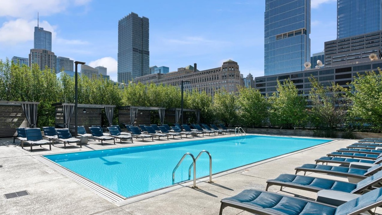 Expansive outdoor swimming pool surrounded by lounge chairs and cabanas, with a Chicago city skyline backdrop at Hubbard Place
