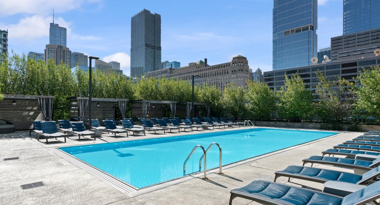 Expansive outdoor swimming pool surrounded by lounge chairs and cabanas, with a Chicago city skyline backdrop at Hubbard Place