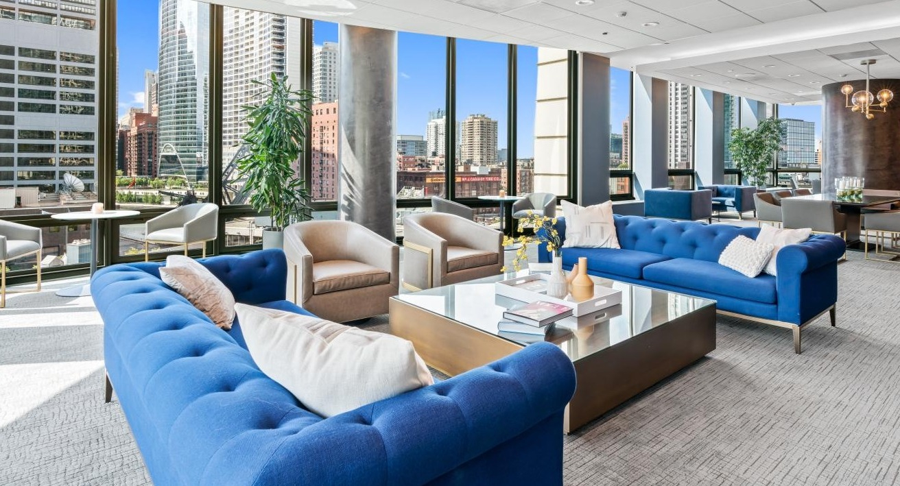 Expansive resident lounge with vibrant blue sofas, comfortable chairs, and panoramic city skyline views at Hubbard Place in Chicago