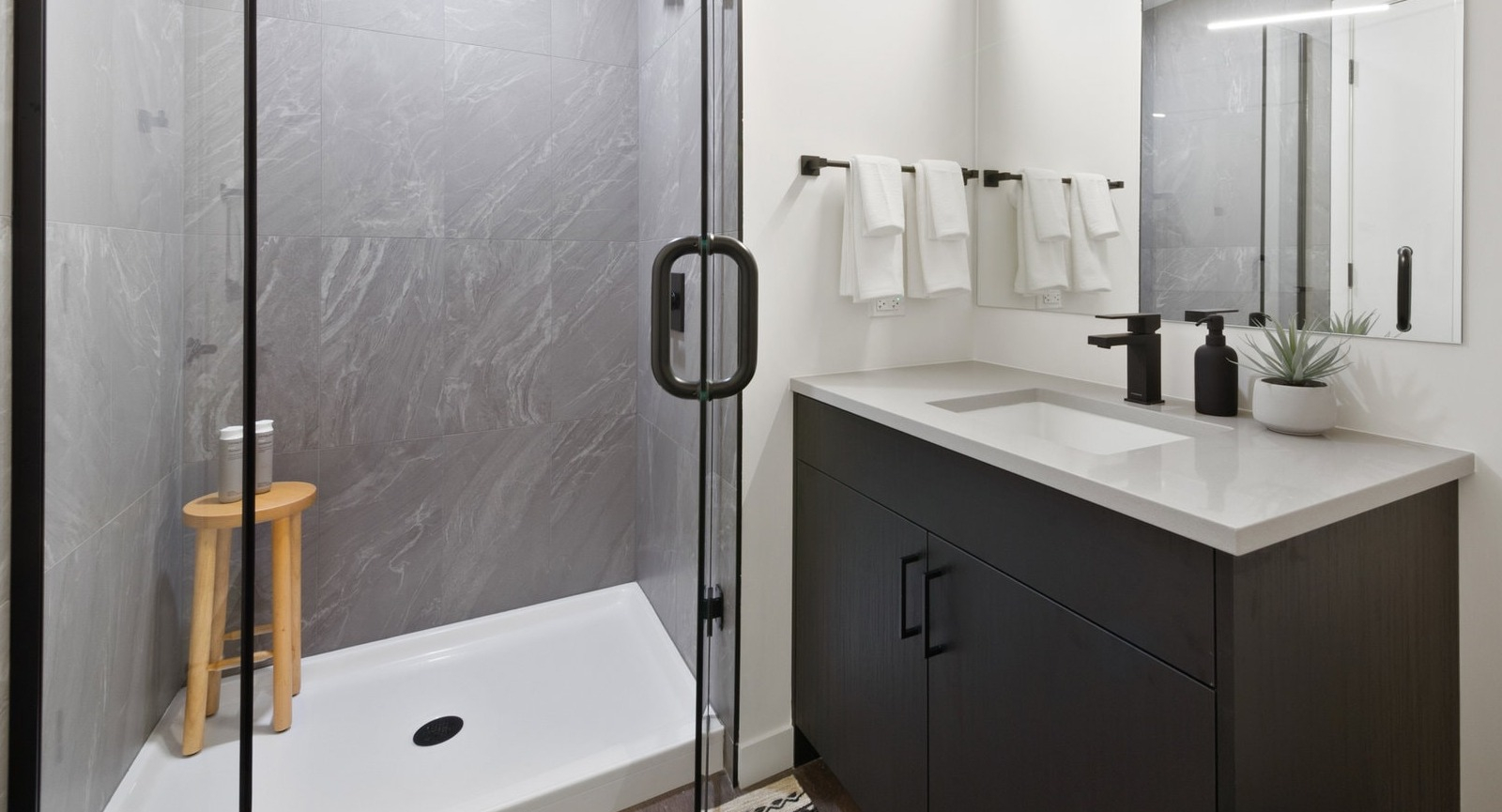 Contemporary bathroom featuring a dark vanity, modern mirror, and a spacious walk-in shower with grey tiles at Hugo Apartments River North, Chicago