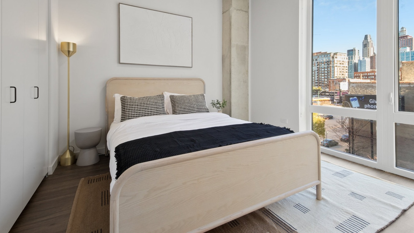 Cozy bedroom with minimalist decor, hardwood floors, and large windows providing city views at Hugo Apartments River North, Chicago