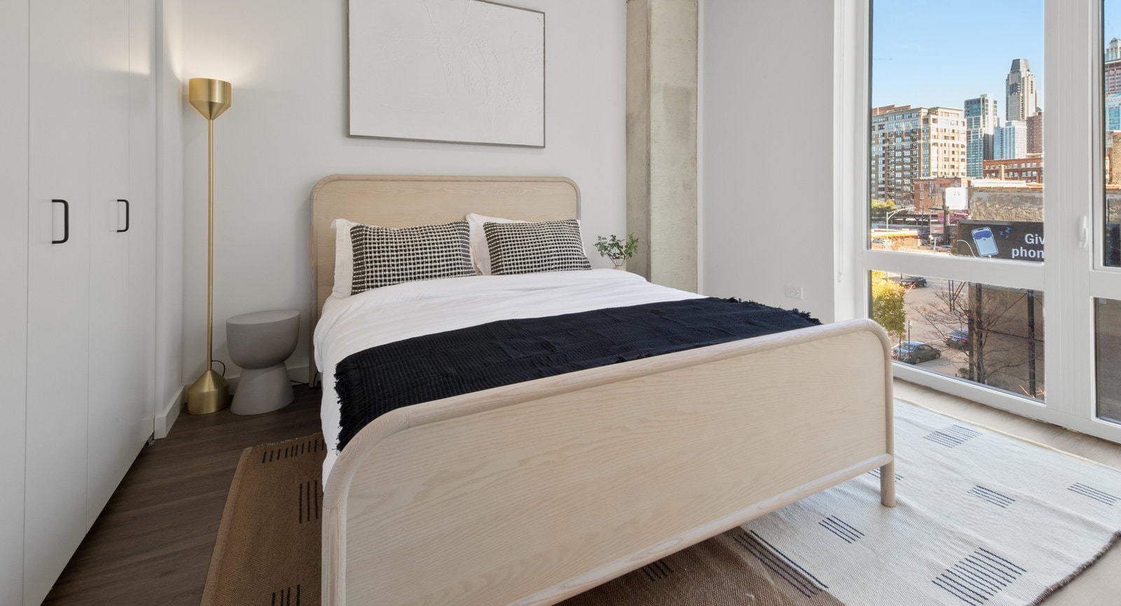 Cozy bedroom with minimalist decor, hardwood floors, and large windows providing city views at Hugo Apartments River North, Chicago
