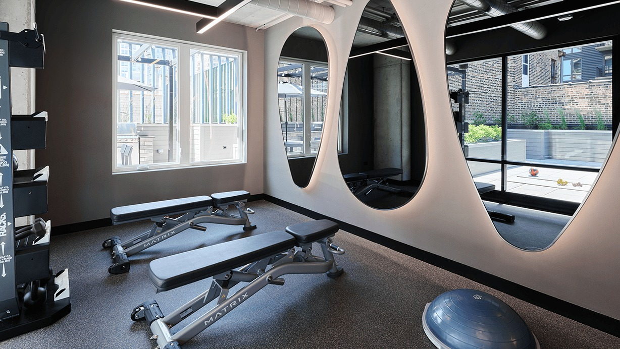 Well-appointed fitness room with free weights, benches, and unique mirrored walls at Hugo Apartments River North, Chicago