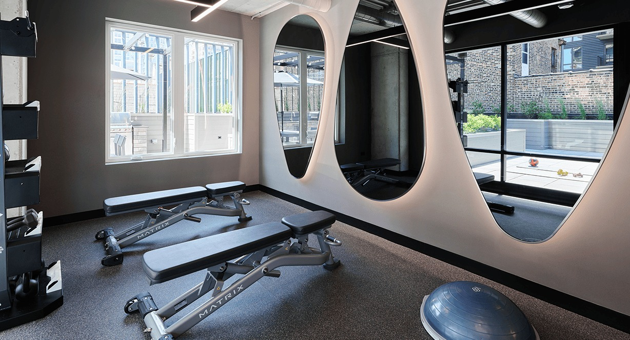 Well-appointed fitness room with free weights, benches, and unique mirrored walls at Hugo Apartments River North, Chicago