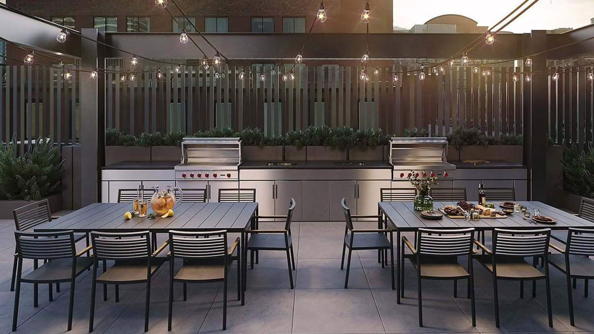 Elegant outdoor dining area with string lights, multiple tables, and modern built-in grills at Hugo Apartments River North in Chicago